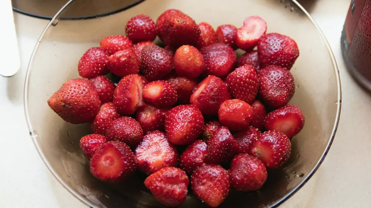 A bowl of fresh strawberries sitting on a kitchen floor next to a golden retriever puppy