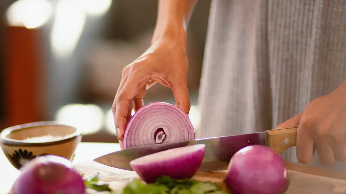 A chopped yellow onion on a cutting board beside a dog looking up from the floor