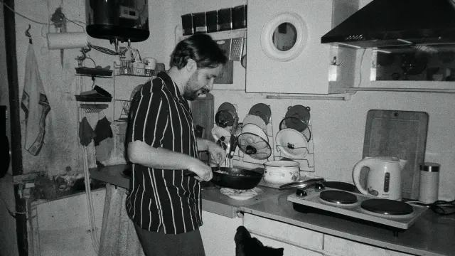 A dog eating from its bowl in a home kitchen while its owner watches nearby