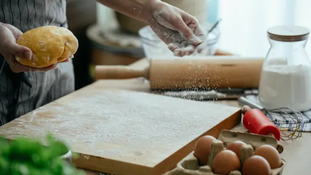 A dog owner sprinkling supplement powder over a bowl of kibble on a kitchen counter
