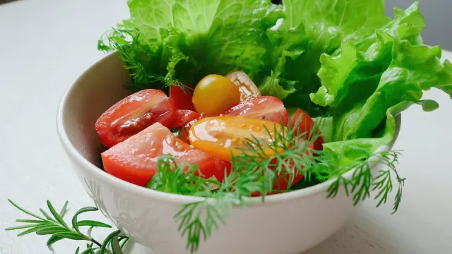 A dog's food bowl beside a small pile of supplement powder and fresh vegetables