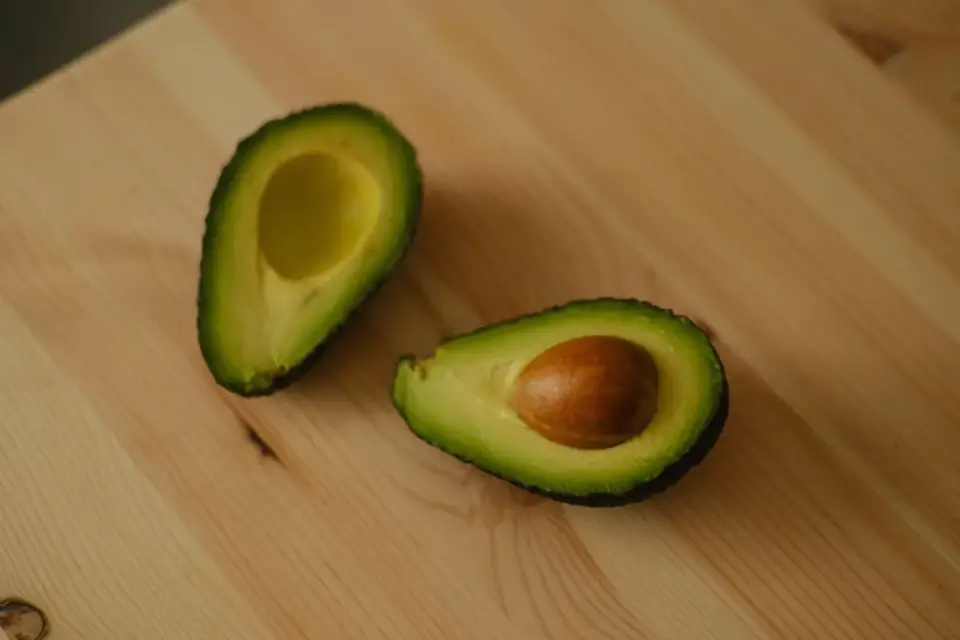 An avocado pit and peeled skin sitting separately from the flesh on a wooden cutting board