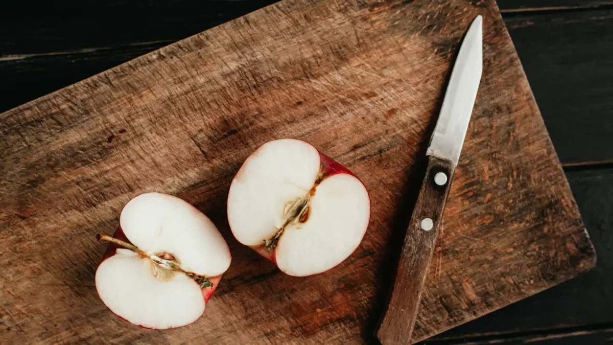 Sliced apple pieces on a cutting board next to a golden retriever resting on a kitchen floor